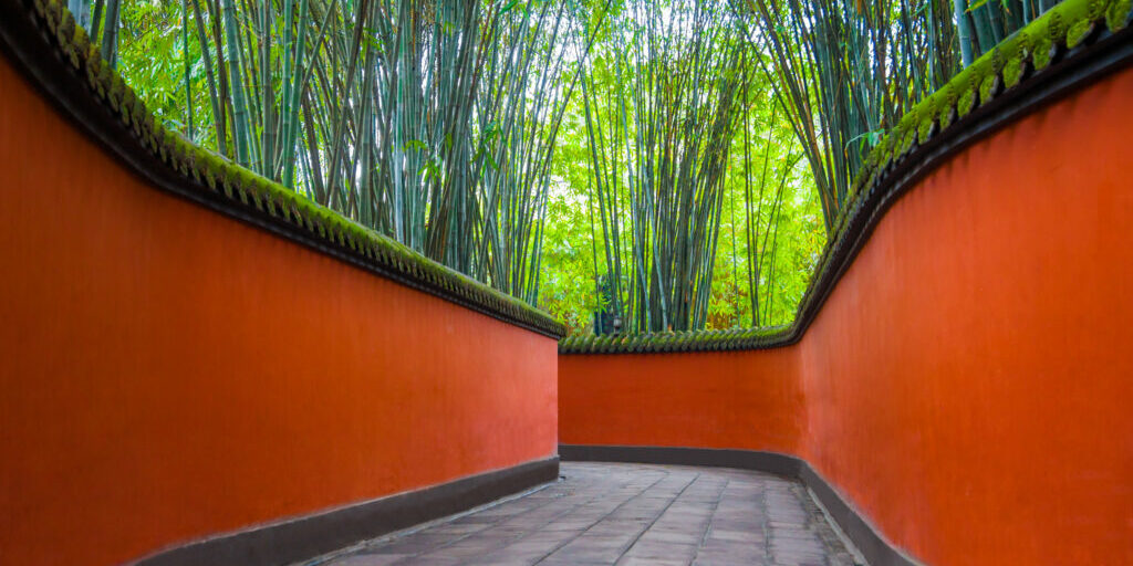Chinesische Allee mit roten Wänden und grünem Bambuswald in Wuhou Temple, Chengdu. Die Anlage hatte die Leute seit the letzten 1780 Jahren faszinierrt und auf diese Weise den Ruf eines heiligen Platzes der Drei Königreiche erworben.